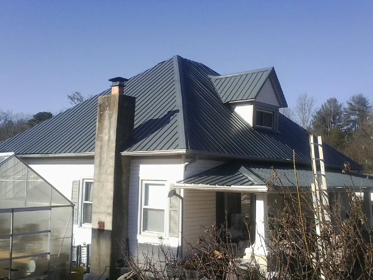 Dark blue standing seam metal roof on a white farmhouse with dormer — Slate & Tile Roof Repair by Roofing Brothers in Saint Thomas