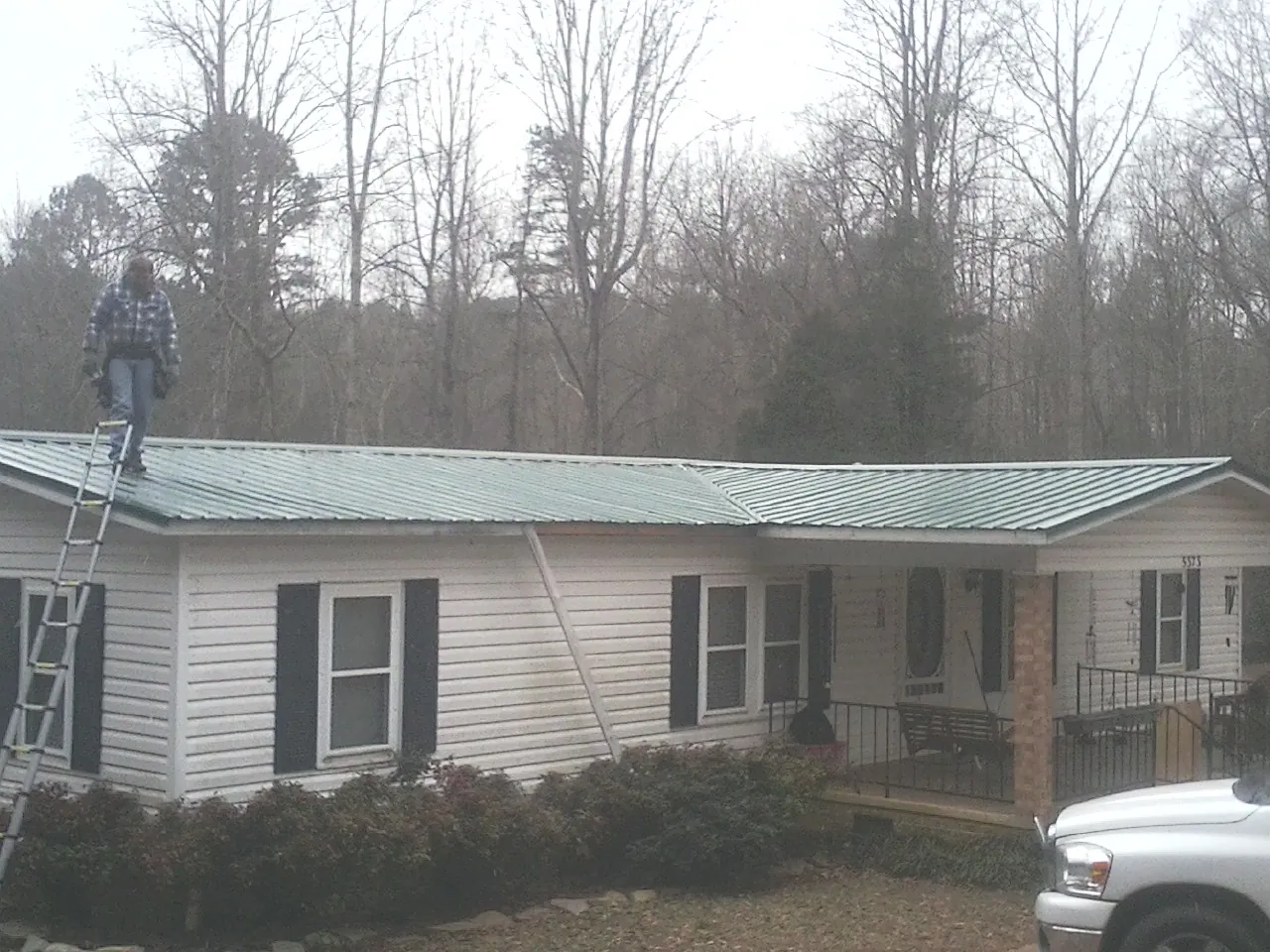Worker on a ladder beside a new green metal roof on a ranch home in Saint Thomas