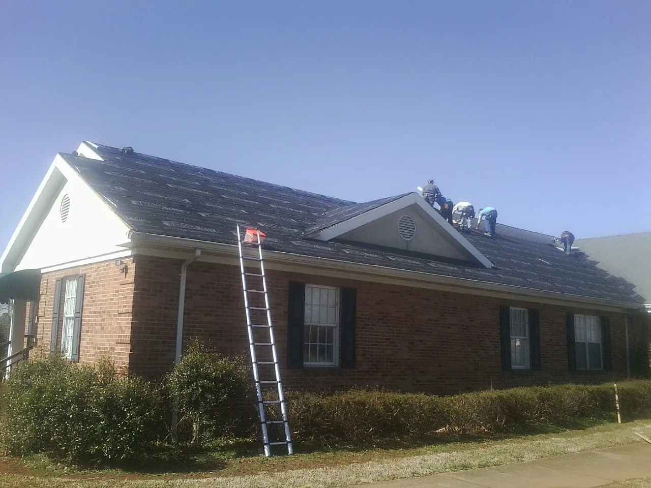 Crew tearing shingles off a brick ranch roof with a ladder set — Emergency Roof Repair work by our crew in Saint Thomas