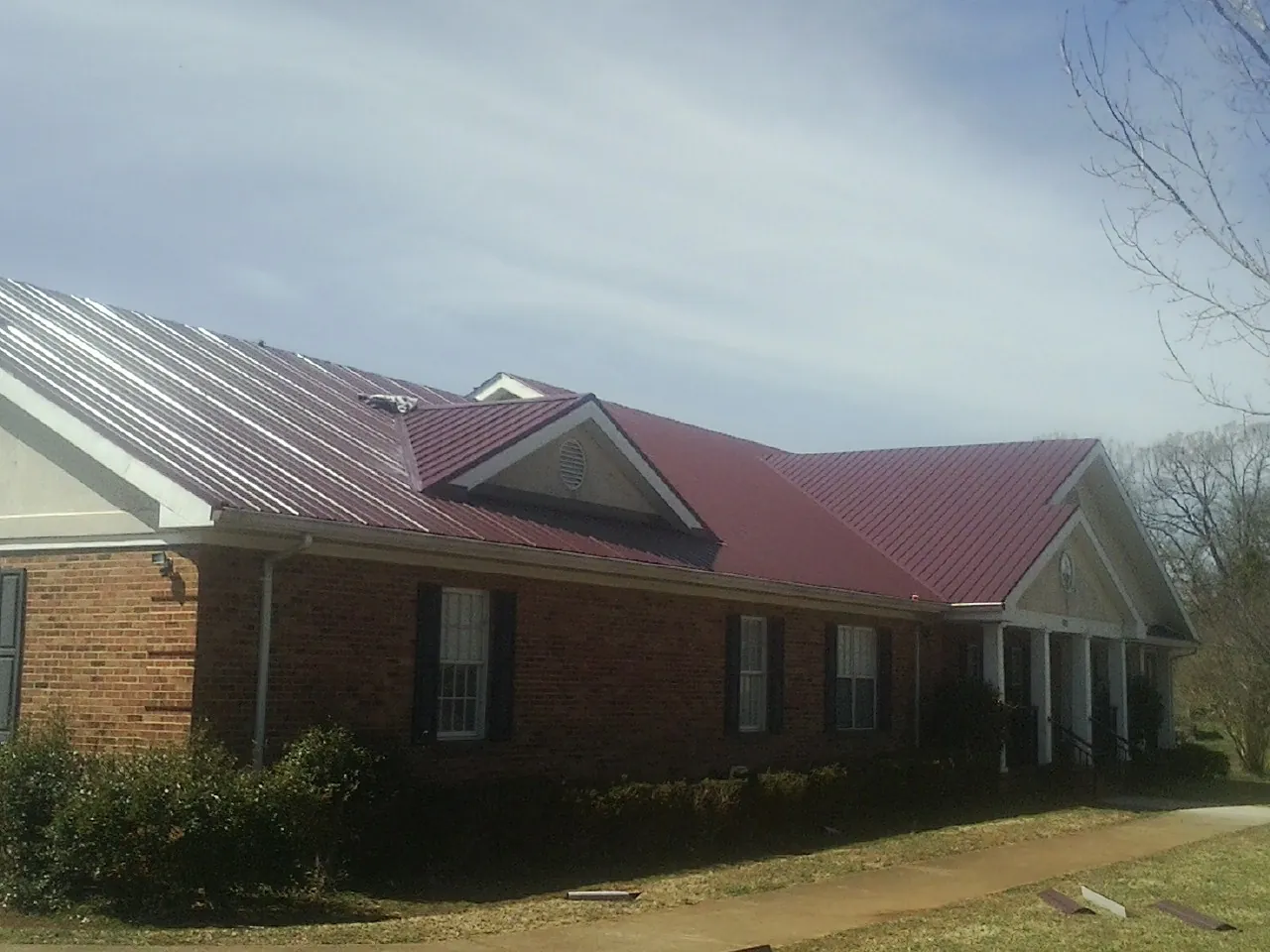 Red metal roof with gabled entries on a long brick building, from a Hail Damage Roof Repair job in Saint Thomas