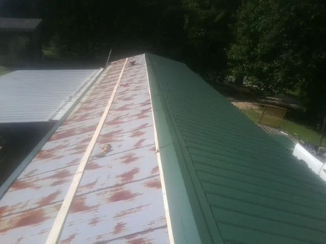 Old rusted panels beside newly installed green metal roofing — Wind Damage Roof Repair by Roofing Brothers in Saint Thomas