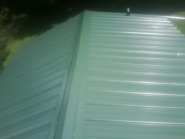 New green metal panels meeting at the ridge of a roof — Flat Roof Repair work by our crew in Saint Thomas