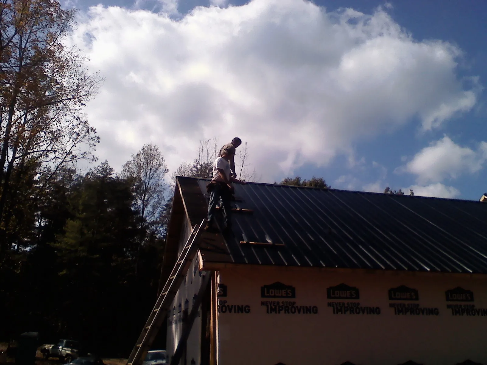 Roofer fastening dark metal panels high against a cloudy sky, from a Roof Inspection job in Saint Thomas