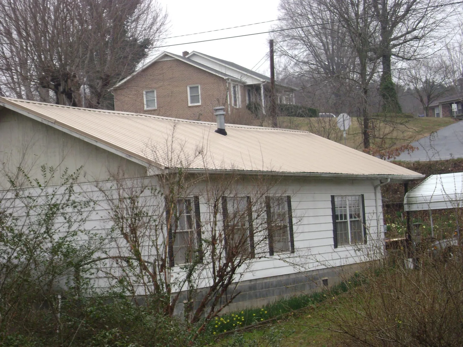 Tan metal roof on a white sided house set into a hillside — Commercial Roofing by Roofing Brothers in Saint Thomas
