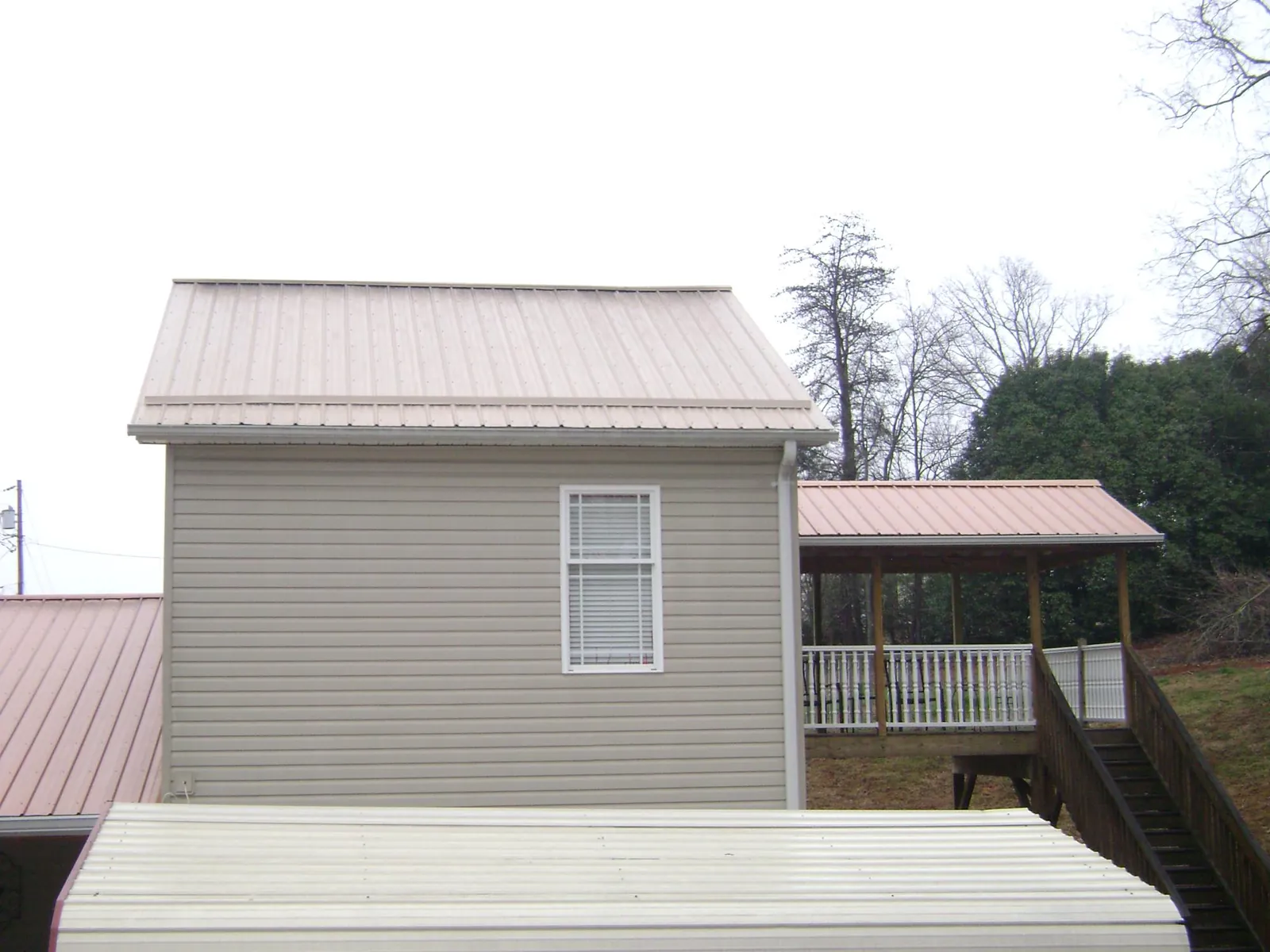 Tan metal roofs on a two story addition and attached porch, from a Roof Replacement job in Saint Thomas